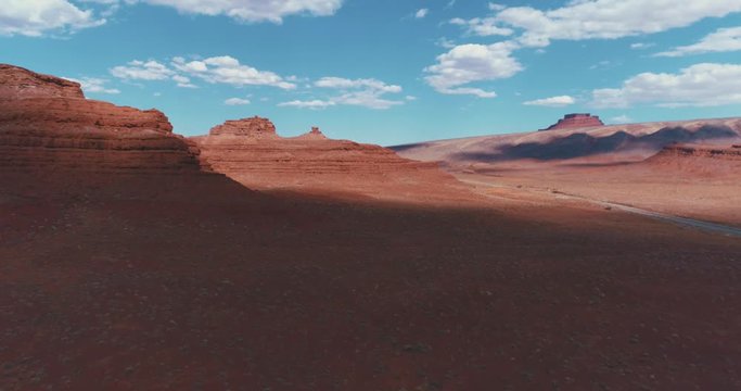 4K UHD DJI Drone Aerial of the famous Monument Valley Navajo National Indian Reserve Park in Utah / Arizona, USA with blue sky and clouds above the red soil.