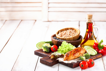 The baked chicken fillet and vegetables. Healthy and fitness food. Meat, salad, vegetables, nuts, beans on a light wooden background. Selective focus. Copy space