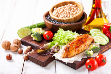 The baked chicken fillet and vegetables. Healthy and fitness food. Meat, salad, vegetables, nuts, beans on a light wooden background. Selective focus. Copy space