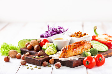 The baked chicken fillet and vegetables. Healthy and fitness food. Meat, salad, vegetables, nuts, beans on a light wooden background. Selective focus. Copy space