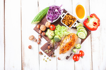 The baked chicken fillet and vegetables. Healthy and fitness food. Meat, salad, vegetables, nuts, beans on a light wooden background. Selective focus. Copy space. Top view