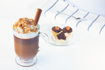 Coffee, cappuccino in a glass, Irish glass. Whipped cream sprinkled with ground nuts and chocolate chips, a cinnamon stick. Glass plate, baskets with chocolate and hazelnuts. The photo.