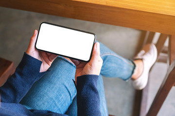Top view mockup image of a woman holding black mobile phone with blank white screen while sitting in cafe
