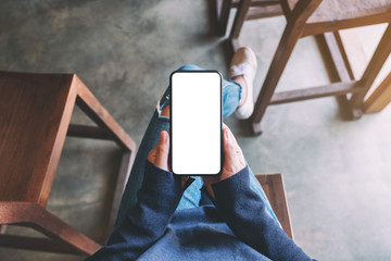 Top view mockup image of a woman holding black mobile phone with blank white screen while sitting in cafe
