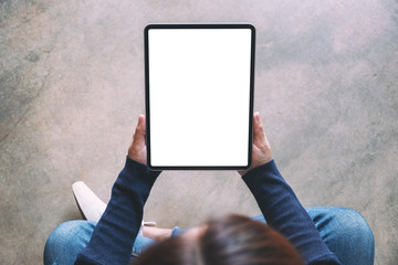 Top view mockup image of a woman holding black tablet pc with blank white screen while sitting on...