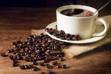 Dark roasted coffee beans and a white cup of coffee on wood table