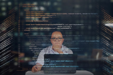 Young IT male student reading his HTML codes projected on a virtual hologram screen with his laptop on the desk. Thinking and focused working at night concept. 