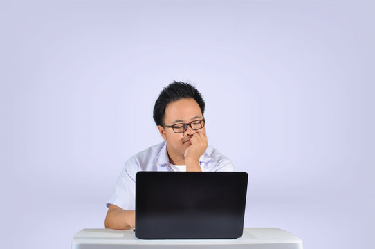 A young Asian student wearing white polo school uniform with eye glasses thinking and analyzing while looking at his laptop screen in white isolated background. 