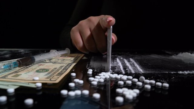 White cocaine powder on a table with dollar bills and a syringe