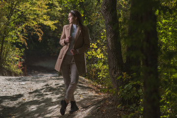 a beautiful, young brown-haired woman in a beige coat and a white turtleneck poses against the background of an autumn alley with yellow and red foliage