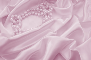 Delicate pink satin draped fabric with natural river pearls for festive backgrounds