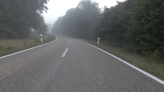 POV Driving on an asphalt road in fog across empty countryside.