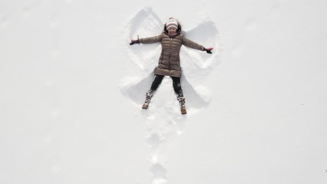 Asian woman playing in the snow and making snow angels.