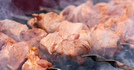 skewers of meat with smoke is cooking on the coals
