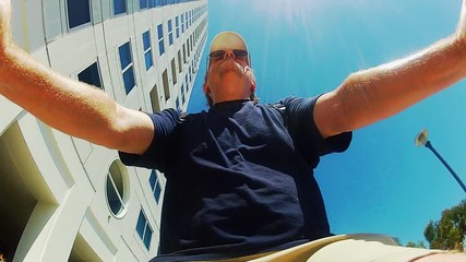 Low Angle- Mature Man Rides Bicycle Under High Rise Building