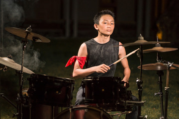 Asian American mixed teenager playing drums at home garden . cool and handsome young boy practicing on drum kit rehearsing passionate in badass rock band look