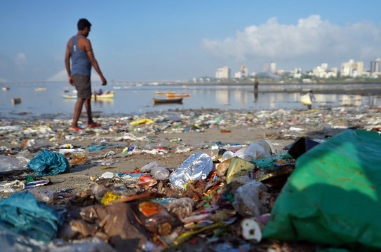 A man walks on a garbage-strewn beach in Mumbai