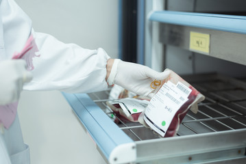 Selective focus scientist hand holding red blood bag in storage blood refrigerator at blood bank...