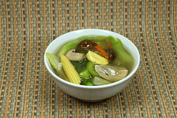Soup of vegetable (carrot, Chinese kale, baby corn and mushroom) in the white bowl. Topping of rice or noodle.