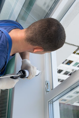 master in protective gloves and blue uniform, closes the cracks of the plastic window with white...