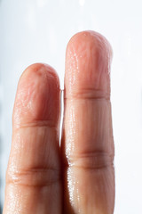 Woman's wet left hand with water drops on middle finger,  White acrylic background, Close up & Macro shot, Selective focus, Asian Body skin part, Relaxing Bath, Healthcare concept