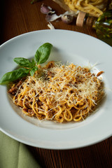 Bolognese pasta with red sauce, parmesan and minced meat. Italian spaghetti with meat in a white plate on a wooden background.