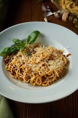 Bolognese pasta with red sauce, parmesan and minced meat. Italian spaghetti with meat in a white plate on a wooden background.