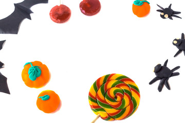 Halloween decoration. Frame from pumpkins and spiders hand made from plasticin, paper bats and candies with copy space on a white wooden background.