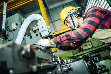 Asian worker wering the goggle, helmet, ear muff equipment in production plant using machine on the factory shop floor