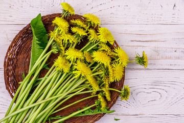 Yellow dandelion flowers in wicker basket on white wooden background. Top view