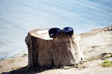 Sunglasses hang on a tree stump, on a background of river with sun highlights