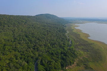 Aerial top view over mountain rural road in tropical rainforest with green tree, road going through forest from above by drone.