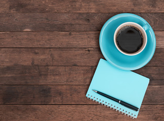 Blue coffee cup,pen and notebook on grunge wooden table top background,top view with copy space