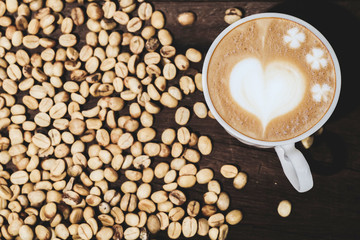 Organic Raw coffee beans with late art coffee cup on wood table.