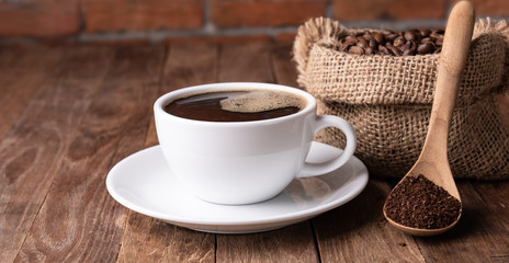 Coffee cup,coffee ground and coffee beans in burlap on wood table with brick wall background