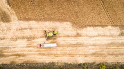 A beautiful new combine harvester dumps grain into a truck trailer on the field. Aerial view