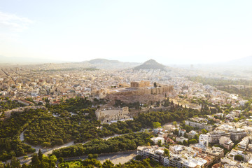 Fototapeta premium Aerial view of a slide from the drone on the panorama of residential buildings of the city of Athens, on the main symbol of ancient Greece, Acropolis at sunrise. The lights sun. World Heritage sites
