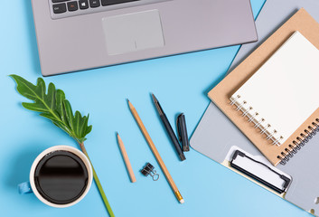 Works pace compositon with coffee cup,document file, notebook, laptop, and green leaves with space on  blue background,top view