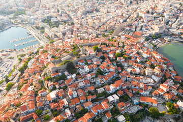 Aerial view of a slide with a drone on a panorama of buildings of residential and administrative houses of the city of Kavala in Greece at dawn. Roof plan from a bird's eye view. Sea. Fortress. Sunset