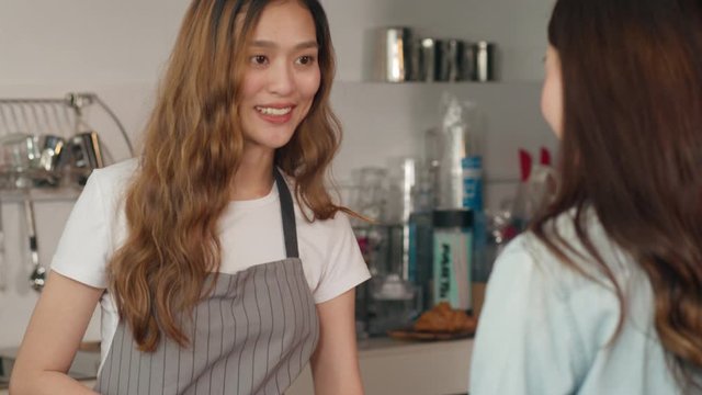 Young Asian woman self service order drink menu with tablet screen at cafe restaurant. Girl barista talking receive orders from customer at bar counter in coffee shop. Owner small business concept.