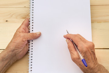 Hands of an elderly man hold a notebook and pen. The concept of writing memoirs, old age and...