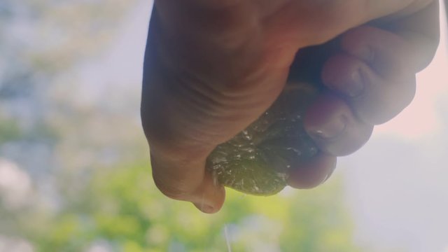 Macro: A Young woman's hands squeeze lime juice out of a lime in a kitchen.