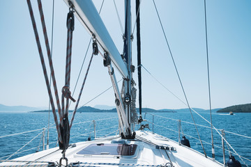 Bow of yacht and yacht equipment. The texture of the masts and ropes on a background of mountain peaks, blue sea and blue sky on a sunny day in summer. Details of sailing equipment. Tourism. Travel