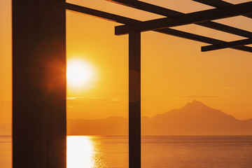 Mount Athos in Greece at sunset a bright sunrise in the early summer morning. Beautiful silhouette of Mount Athos in Greece in the Aegean Sea. Calm seawater surface. Orange disk of the sun and rays