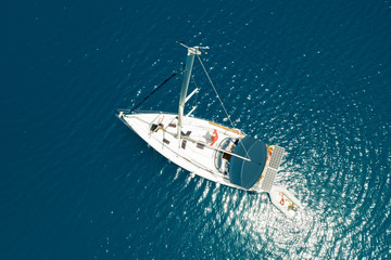 Aerial view of a slide from a drone on a pleasure sailing vessel sailing along the waves over the sea. The texture of the masts and ropes, mountain peaks, blue sea and blue sky in summer