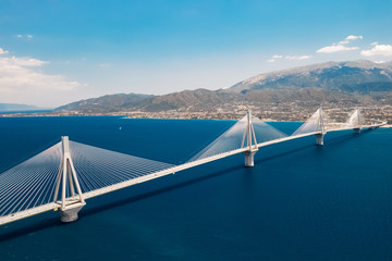 Aerial view from a drone on a beautiful large bridge for a highway across the sea in Patras, Greece. Refined, beautiful design of the bridge. Blue sea and sky. Part of the coast with buildings