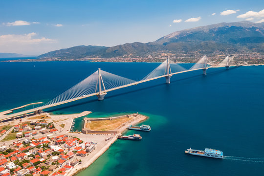 Aerial view from a drone on a beautiful large bridge for a highway across the sea in Patras, Greece. Refined, beautiful design of the bridge. Blue sea and sky. Part of the coast with buildings - Powered by Adobe