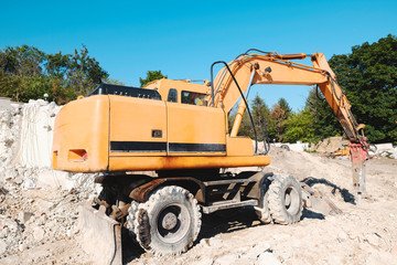 A large yellow construction equipment is digging a pit for the base of a residential complex with an industrial jackhammer. Construction of a large residential building. Initial construction phase