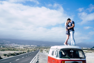 Young couple in love enjoying the travel on a vintage van standing on the roof and hugging with...