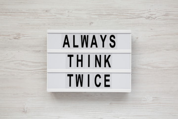 'Always think twice' words on a lightbox on a white wooden background, top view. Overhead, from above, flat lay.